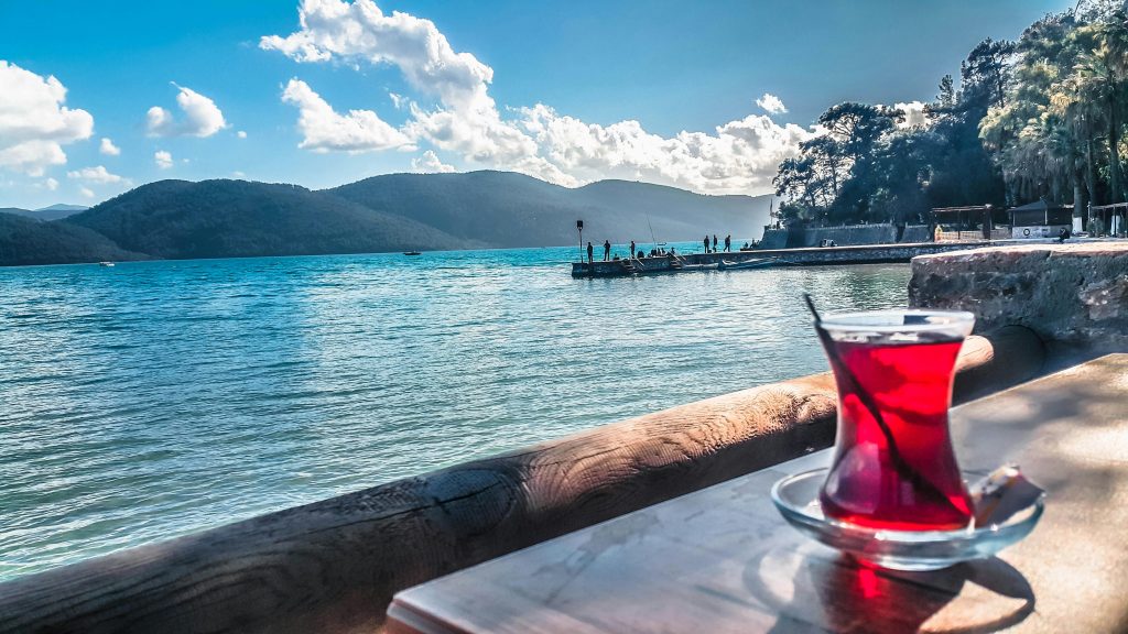 a glass of red liquid on a table by a body of water